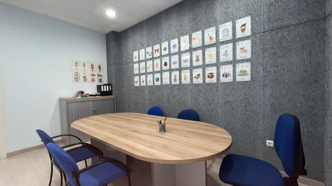 Imagen de sala para grupos con mesa ovalada grande rodeada de sillas y carteles con letras infantiles y del cuerpo humano en la pared