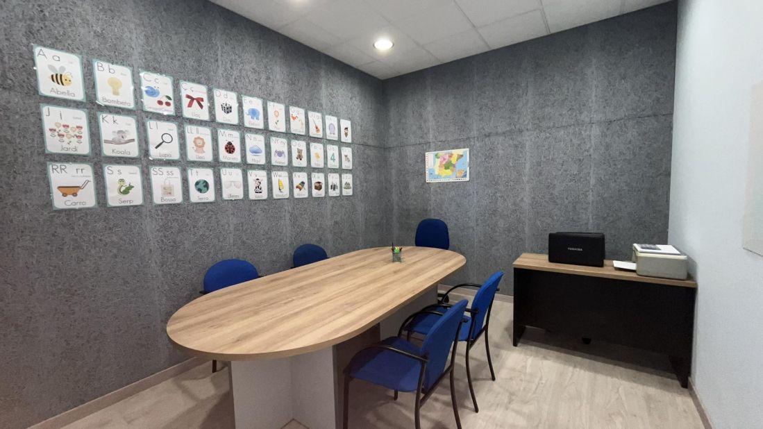 Imagen de sala para grupos con mesa ovalada grande rodeada de sillas y carteles con letras infantiles en la pared