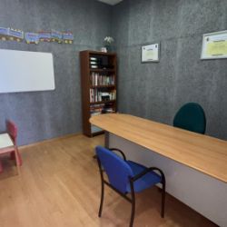 Imagen de sala de entrada con mesa larga, dos sillas enfrentadas y una mesa infantil en la esquina